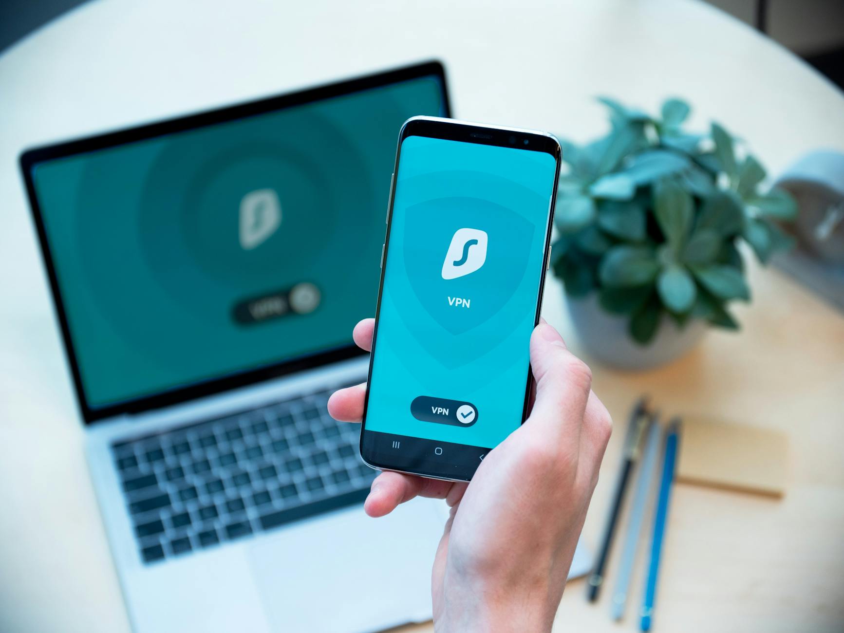 Smartfon z uruchomioną aplikacją VPN trzymany w dłoni przed laptopem