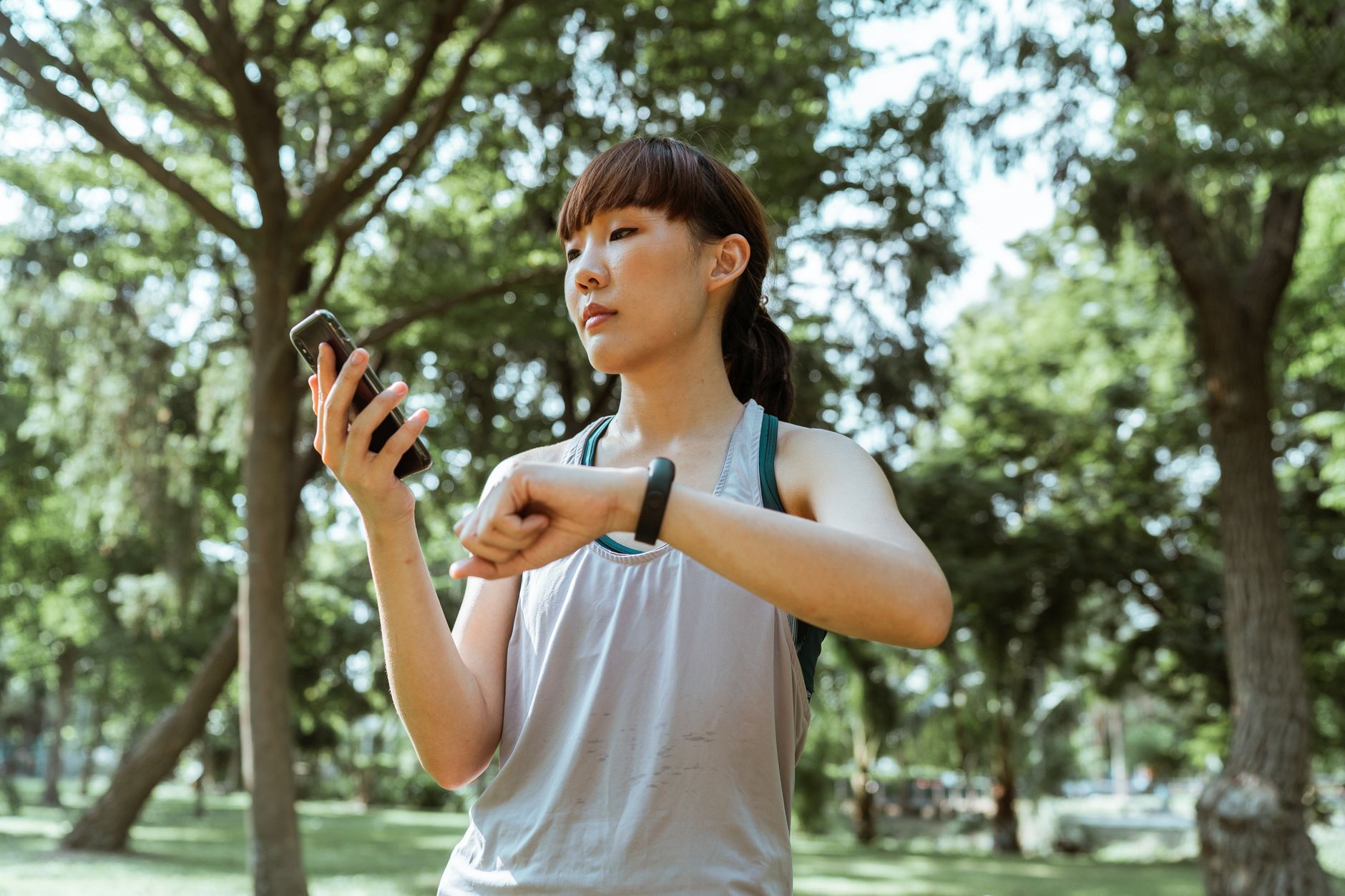Azjatycka sportsmenka sprawdza opaskę fitness i smartfon w parku