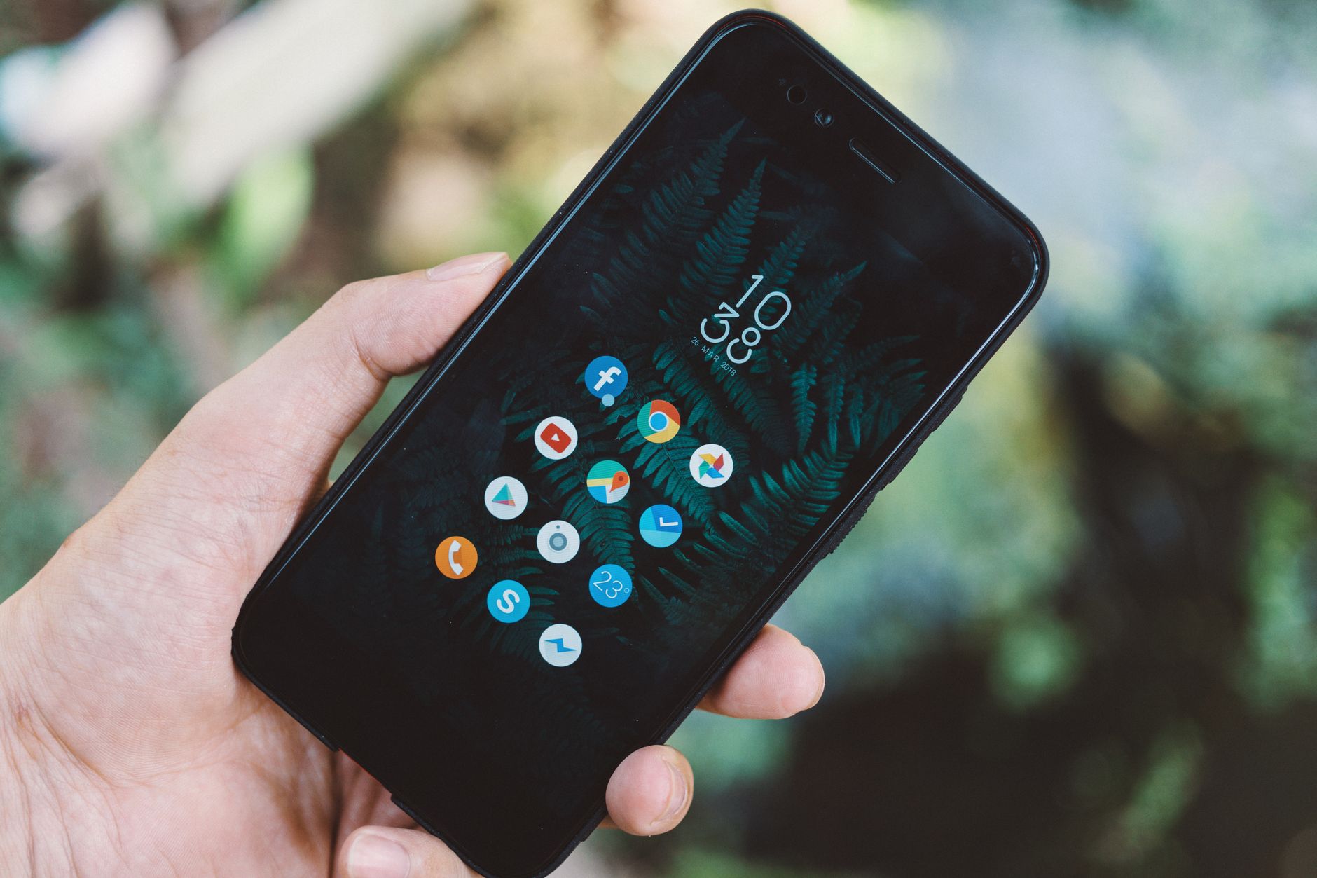 Dłoń trzymająca smartfon z ikonami aplikacji na tle natury