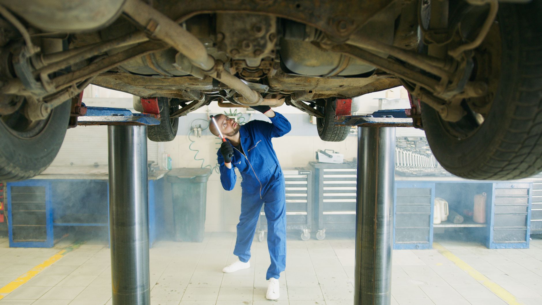Mechanik w niebieskim kombinezonie sprawdza auto na podnośniku w warsztacie