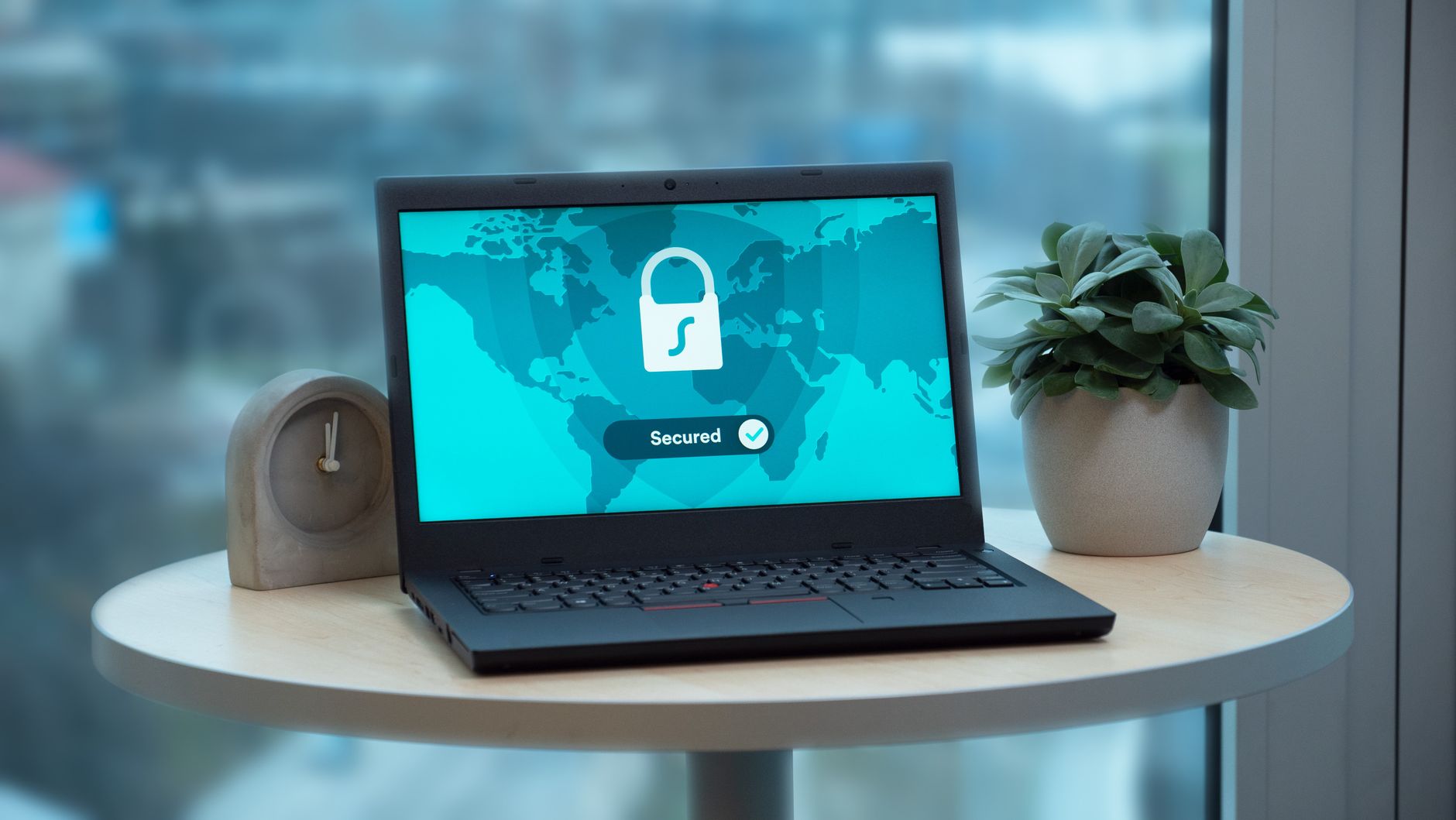 Laptop z ikoną kłódki bezpieczeństwa na stole obok rośliny i zegara