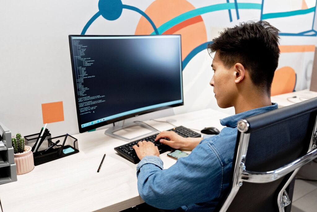Programista pracujący nad kodem przy biurku z dużym monitorem