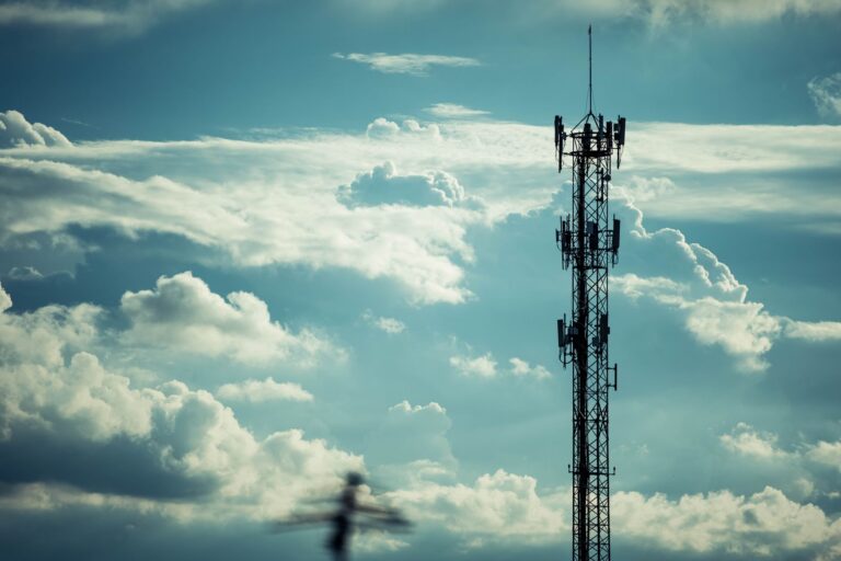 Sylwetka wysokiego masztu telekomunikacyjnego na tle jasnego, pochmurnego nieba